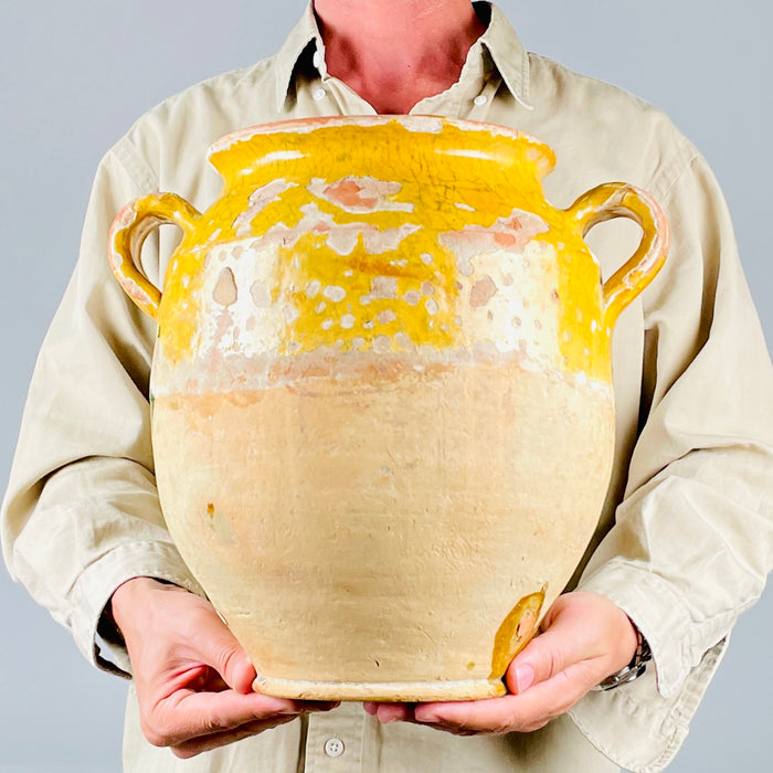 Large French confit pot in antique terracotta, notable for its scale, broad rounded body, and double-handle form. The honey-yellow glaze remains strongest around the shoulder and interior, while the lower body shows exposed clay and gentle wear. This 19th century French pottery jar has the rustic presence sought for farmhouse decor, French country decor, and antique pottery displays.