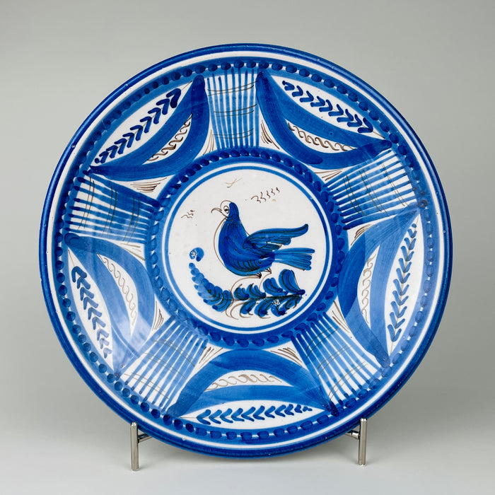 Antique Spanish majolica wall plate from early 20th century Talavera de la Reina, formed as a shallow tin glazed earthenware charger and hand painted in cobalt blue with manganese brown accents. A stylized bird stands on a leafy branch within concentric bands of foliate arcs, lattice panels, dots, and linear ornament, creating strong Mediterranean decor.