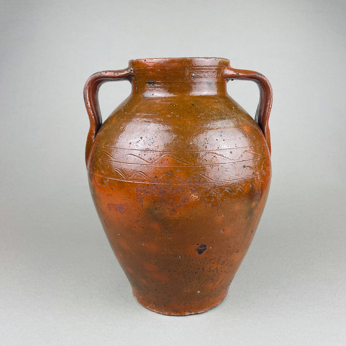 Antique terracotta pot with twin handles, warm red clay body, and a glossy brown slip glaze that pools around the shoulder and neck. The ovoid form and wide mouth read as a decorative vase for vintage home decor, styled as farmhouse decor or French country decor with wood, linen, and natural tones.
