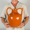 Antique French folk art jug with an open filling mouth and hollow tubular spout, identifying its traditional function as a gargoulette water vessel. Wheel thrown in terracotta during the early 1900s, its glossy brown glaze, exposed red clay and handmade asymmetry give it strong vernacular pottery character.