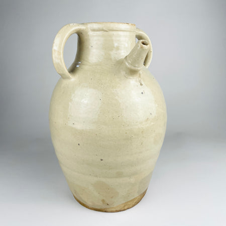 Large antique French white cruche pot from the early 20th century, wheel thrown in glazed terracotta with a rounded body, broad neck, twin loop handles and an applied pouring spout. The cream and ivory surface shows dark mineral specks, age variation and an unglazed foot; the decorative vessel measures 32 cm tall.