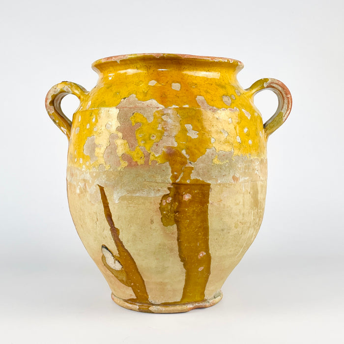 French terracotta confit pot with antique yellow glaze, showing the sculptural ovoid body and practical storage jar form associated with old French kitchen pottery. The vessel displays pronounced wear, glaze losses, and age-softened texture across the shoulder and rim. As an antique pottery jar, it fits farmhouse decor, rustic decor, and Mediterranean decor with authentic character