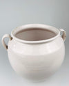 Antique French white confit pot in glazed faience from Martres Tolosane, with a thick curved handle applied to the shoulder and a softly flared rolled lip above. Small glaze chips expose the warm buff ceramic body beneath, adding honest age character to a substantial regional pot à graisse for farmhouse decor.