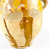 Antique French confit pot in pottery and terracotta, with yellow glaze, rolled rim, and distinctive hand-applied handle detail. The surface cararies heavy patina, glaze crazing, and worn patches that emphasize age and handmade construction. This organic decorative vessel suits wabi sabi decor, French country decor, and rustic interiors where weathered materials and antique pottery are central.