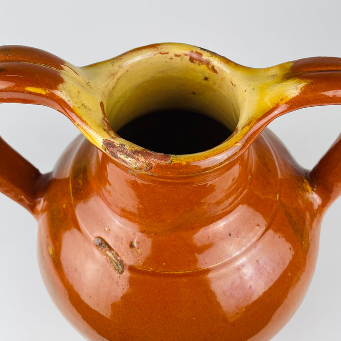 Large brown pottery jug from southern France with the functional shape of a traditional water gargoulette. The applied loop handle supported carrying, while the raised open spout allowed controlled pouring. Yellow glaze around the mouth contrasts with the reddish body for warm farmhouse decor and antique kitchen display.