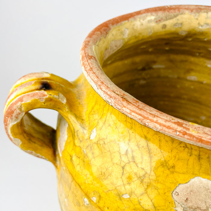 Antique French confit jar in terracotta and pottery, with a broad shoulder, rounded belly, and loop handles typical of historic preserving vessels. The glaze has worn beautifully across the upper body, revealing layers of cream, ochre, and clay tones. This provincial French jar functions as decorative pottery for French country decor, rustic home decor, or a statement terracotta vessel.