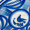 Central decoration on the Spanish Talavera wall plate depicts a stylized cobalt blue bird standing over a plume shaped branch, outlined and feathered with fine manganese brown strokes. The motif sits within double blue rings on a white tin glazed ground, giving this antique faience bird plate a clear focal point for botanical wall art.