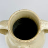 Antique white terracotta water jug from France with concentric throwing lines visible through the glossy cream glaze. Small iron-colored specks and tonal patches animate the generous body, while the twin handles and compact pouring spout preserve the recognizable form of a traditional cruche or pottery vase.