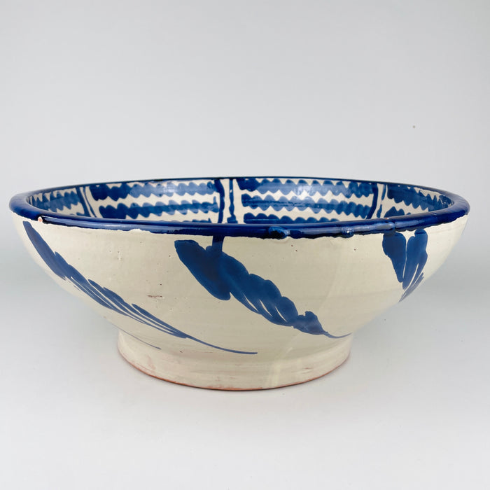 Vintage Spanish Fajalauza bowl from Granada in glazed earthenware, featuring a cream white ground with bold cobalt blue decoration. The interior shows a central floral medallion surrounded by rhythmic wavy bands, while the large basin shape gives it strong presence as a ceramic centerpiece, wall hanging bowl, or decorative accent in Mediterranean decor and French country decor.
