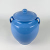 Blue lidded pottery jar from Martres Tolosane, made in France during the mid 20th century as a traditional confit preserving pot. The cornflower glaze follows the curved shoulders and tapered base, while the cream lip outlines the opening, creating a graphic two-tone detail for wabi sabi decor or a ceramic collection.