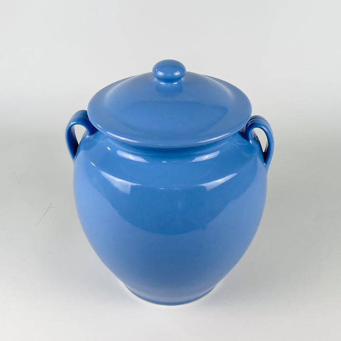 Blue lidded pottery jar from Martres Tolosane, made in France during the mid 20th century as a traditional confit preserving pot. The cornflower glaze follows the curved shoulders and tapered base, while the cream lip outlines the opening, creating a graphic two-tone detail for wabi sabi decor or a ceramic collection.