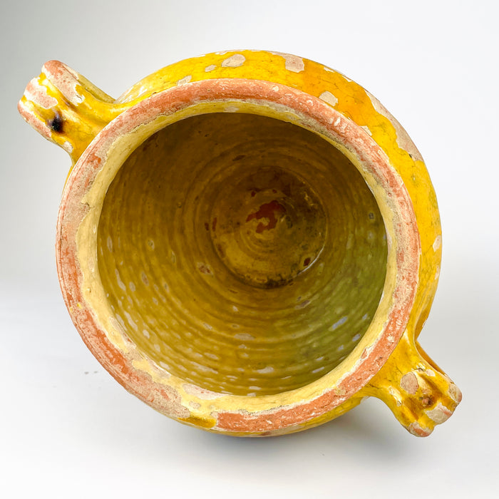 French yellow glazed confit pot in antique terracotta, a rustic kitchen vessel with strong sculptural character. The interior glazing and upper glaze band contrast with the unglazed lower body, a hallmark of traditional French pottery jars. With its loop handles, warm ochre tones, and age-softened finish, it works beautifully in farmhouse decor, country kitchen decor, and Mediterranean decor.