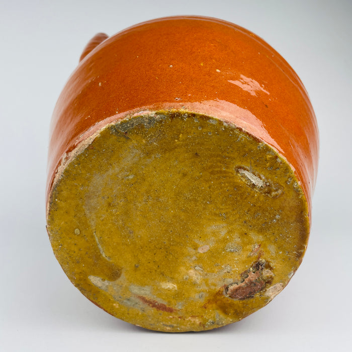 French provincial pottery water vessel made in Southwest France during the early 20th century. The gargoulette form combines practical volume with a high handle and large hollow spout, while yellow glaze inside the mouth and reddish brown glaze across the body create a rich two tone ceramic surface.