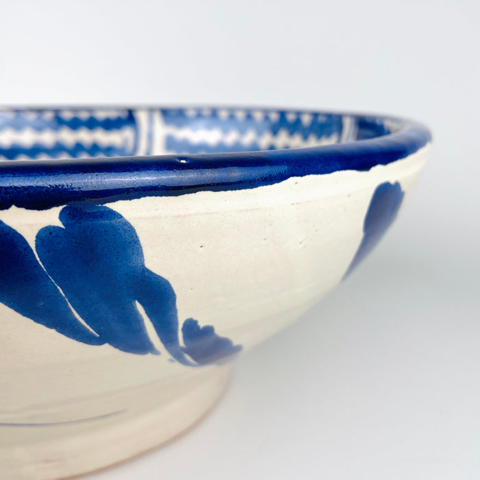 The broad circular scale of this Spanish Fajalauza bowl emphasizes its substantial presence as a decorative object. Hand painted cobalt blue waves, a central sunflower, and scrolling foliage fill the white glazed interior, while the traditional lebrillo depth gives the piece sculptural volume. It works as statement wall art, a fruit bowl, or a large table centerpiece for Mediterranean decor and vintage home decor.