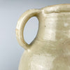Early 1900s French cruche pot formed on a potter’s wheel from fired clay and covered in an irregular cream glaze. The broad cylindrical neck, symmetrical loop handles and small projecting spout identify its traditional household vessel form, while its generous scale gives this antique pottery strong decorative presence.