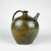 An antique French green glazed pottery jug with a rounded body, curved handle and tubular spout. The supplied measurement label states a height of 27 centimetres, a width of 25 centimetres and a weight of 2.4 kilograms. Olive and brown glaze contrasts with small areas of exposed orange clay on this substantial terracotta vessel.