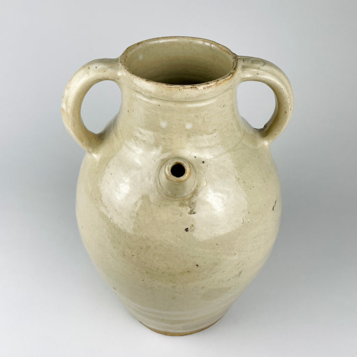 Early 20th century French white pottery vessel with a broad open neck, rounded rim and twin carrying handles. The softly uneven glaze ranges from ivory to pale beige and retains mineral flecks, gentle rubbing and traces of age that complement wabi sabi decor without obscuring the cruche’s strong utilitarian form.