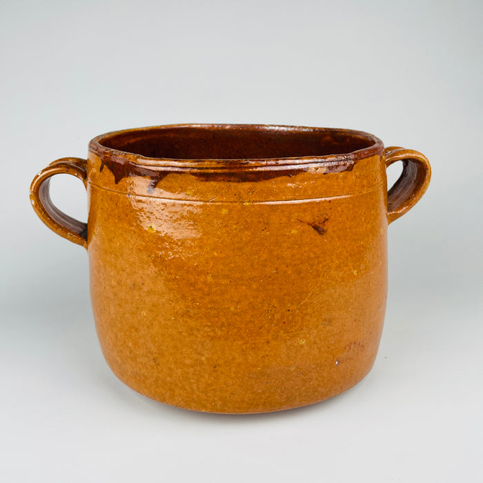 Upper body and second loop handle of the signed Vallauris cooking pot, showing the dark rim glaze, honey mustard earthenware surface and natural glaze variation from historic use. The substantial two-handled form identifies this as an antique French marmite crock with lid and distinctive Provence pottery character.