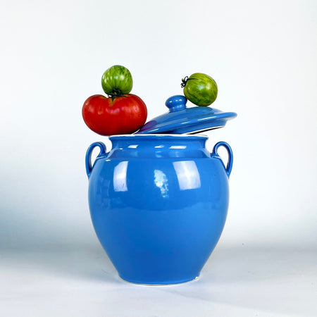 Vintage French faience confit pot with a fitted domed lid and rounded knob, finished in a luminous blue glaze over a full, softly tapering body. Twin handles flank the short neck, while subtle production irregularities connect this Martres Tolosane preserving jar to French provincial pottery and collected vintage home decor.