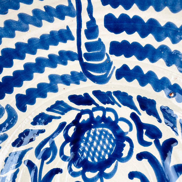 The broad circular scale of this Spanish Fajalauza bowl emphasizes its substantial presence as a decorative object. Hand painted cobalt blue waves, a central sunflower, and scrolling foliage fill the white glazed interior, while the traditional lebrillo depth gives the piece sculptural volume. It works as statement wall art, a fruit bowl, or a large table centerpiece for Mediterranean decor and vintage home decor.