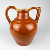 Early 1900s French water pitcher made from red earthenware with a glossy caramel brown glaze and yellow glazed opening. This substantial gargoulette combines an ovoid storage body, sturdy applied handle and raised pouring tube, representing functional French folk pottery with authentic chips, scratches and exposed clay.