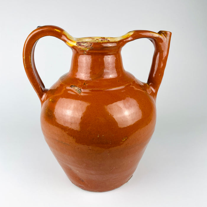 Early 1900s French water pitcher made from red earthenware with a glossy caramel brown glaze and yellow glazed opening. This substantial gargoulette combines an ovoid storage body, sturdy applied handle and raised pouring tube, representing functional French folk pottery with authentic chips, scratches and exposed clay.