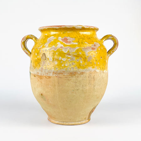 Antique French confit pot in yellow glazed terracotta, a large 19th century pottery jar with rounded body, flared rim, and small applied loop handle. The upper section carries warm ochre glaze with visible craquelure and glaze loss, while the lower body remains unglazed and pale. This French country pottery piece suits farmhouse decor, Mediterranean decor, and rustic home decor.