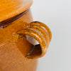 Applied loop handle on the large antique French confit pot, with hand-formed ridges, amber brown glaze, small losses and age-related wear visible around the attachment. This detail shows the craftsmanship and patina of a Foucard Jourdan Vallauris terracotta marmite made as durable wood fire cookware in Provence.