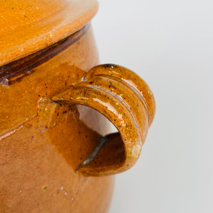 Applied loop handle on the large antique French confit pot, with hand-formed ridges, amber brown glaze, small losses and age-related wear visible around the attachment. This detail shows the craftsmanship and patina of a Foucard Jourdan Vallauris terracotta marmite made as durable wood fire cookware in Provence.