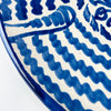 Blue and white Spanish lebrillo bowl from Granada, hand painted with a stylized sunflower and scrolling botanical motifs at the center, surrounded by concentric bands of irregular cobalt waves. The rounded basin, painted rim, and raised foot preserve the traditional form of Fajalauza pottery. It can be used as a decorative wall hanging, fruit bowl, or table centerpiece in farmhouse decor and Mediterranean decor.