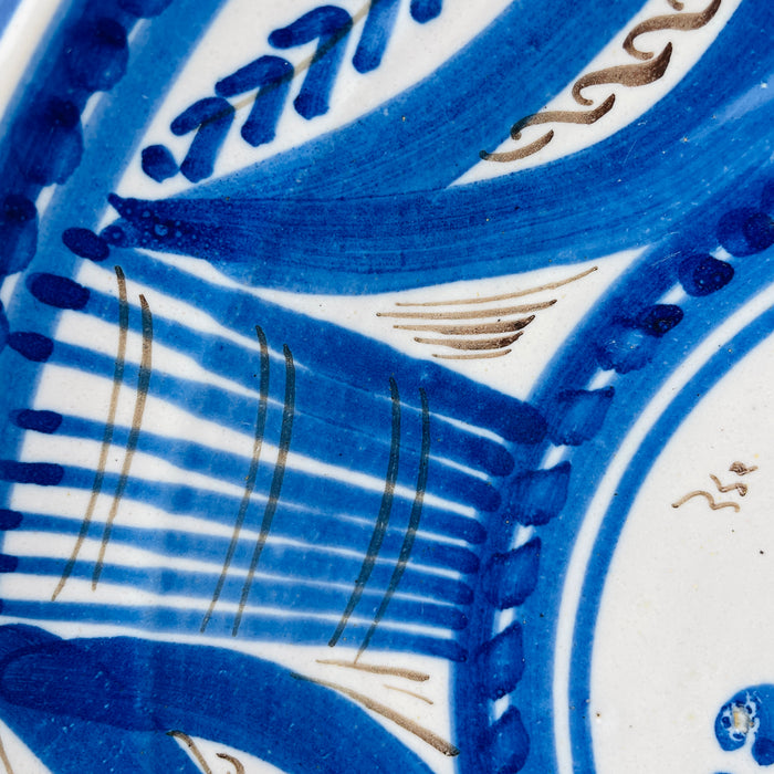 antique Spanish majolica plate measuring 29.5 cm wide, with a cobalt bird framed by dense radial geometry on white glazed earthenware. Its scale is clear when held, while the deep shallow bowl form and bold hand painted pattern allow the Talavera charger to anchor a collected plate wall or eclectic decor scheme.