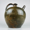 An antique French green glazed pottery pitcher has a generous rounded body and broad loop handle rising to the short neck. The separate tubular spout and narrow incised band distinguish its practical design. Visible glaze losses and earthy terracotta colour give this historic storage vessel a textured appearance suitable for rustic home decor.