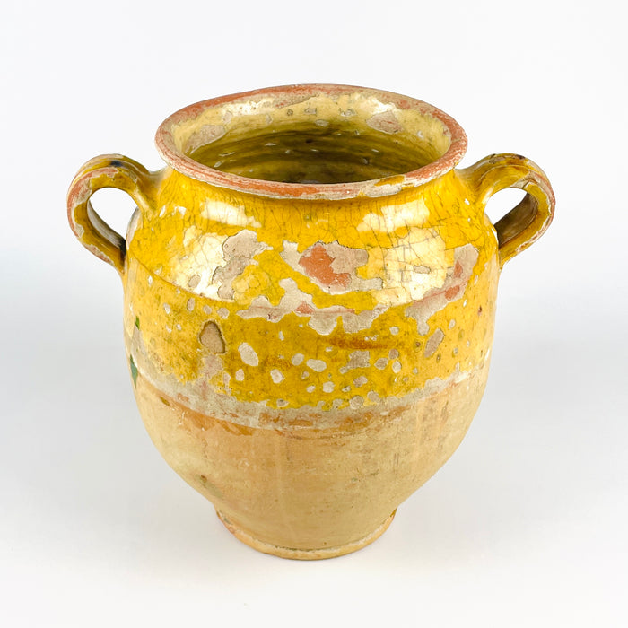Antique French terracotta jar with yellow glaze and traditional confit pot form, combining a practical storage shape with rich decorative appeal. The hand-thrown body, compact foot, and loop handles support its identity as rural French earthenware. Styled as a kitchen decor piece, vase, or standalone object, it brings warmth to French country decor and Mediterranean-inspired spaces.