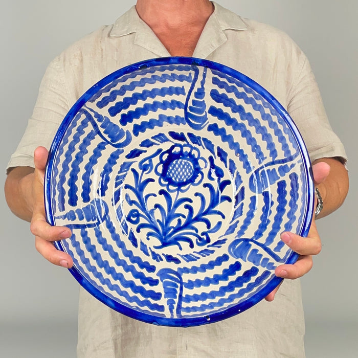 Large hand painted ceramic bowl from Granada, Spain, shaped as a traditional lebrillo with a wide open basin and raised foot. Cobalt blue wave bands radiate around a stylized sunflower and scrolling vegetal forms, while the white glazed ground highlights the expressive brushwork. The piece brings a strong Spanish pottery accent to Mediterranean decor, French country decor, vintage kitchen displays, and cottage decor.