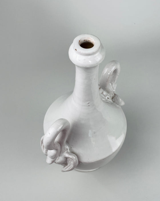 Vintage Italian white pottery vase showing both high looping swan handles balanced against the tall narrow neck and rounded amphora body. The ivory glazed earthenware surface has gentle tonal variation and firing specks, while the classical proportions suit mid century modern decor when used as a sculptural statement rather than a strictly modernist vessel.