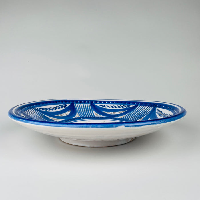 Large Spanish blue bird plate in hand painted Talavera faience, with a white tin glazed ground and a broad cobalt border arranged in alternating leaf shapes, gridded panels, dotted bands, and fine brown scrolls. The shallow charger form and graphic bird motif make this antique pottery a substantial piece of Spanish wall decor.