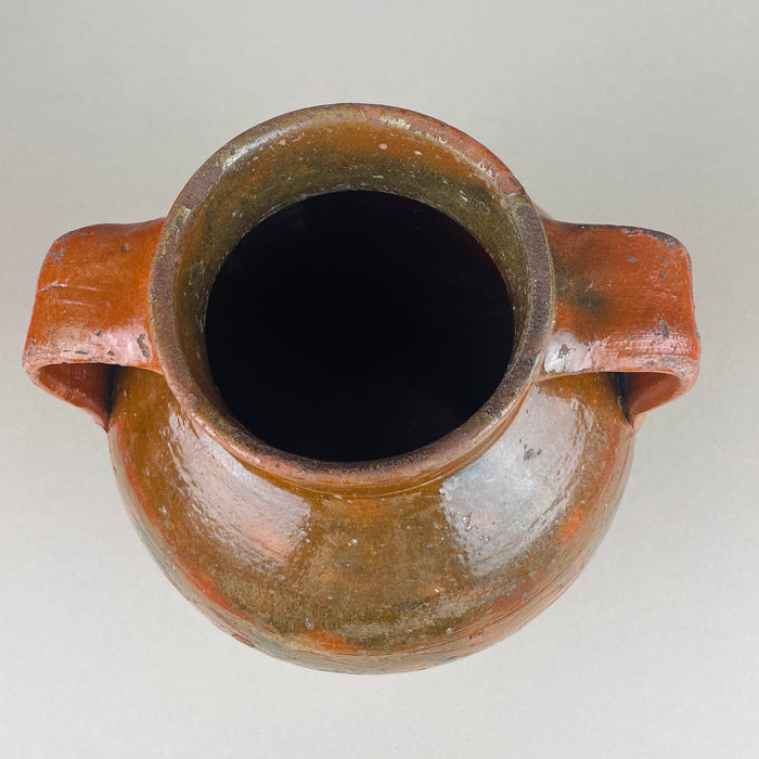 High-angle view of the antique terracotta pot showing the wide mouth, thick rim, and symmetrical twin handles. The glossy glaze catches light across the shoulder while the lower clay remains more matte and tactile. Use as a decorative vase for branches in Japandi or wabi sabi interiors.