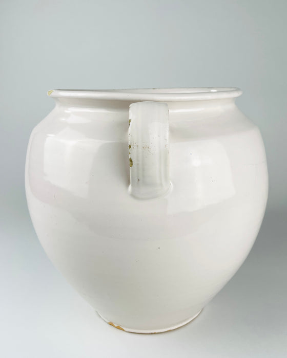 Antique French white confit pot from Martres Tolosane with a generous ovoid body that narrows toward a defined circular foot. Made in glazed earthenware in the early 20th century, the ceramic jar has an opaque cream-white finish, broad rolled lip and balanced loop handles suited to use as a large vase or cottage decor accent.