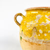 Antique French confit pot in handmade pottery with yellow glaze over the upper body and interior, paired with an unglazed lower half in pale clay. The twin-handle form, rounded profile, and worn terracotta surface identify it as a classic French preserving jar. This decorative antique vessel works as French pottery decor, a rustic vase, or a sculptural accent in country interiors.
