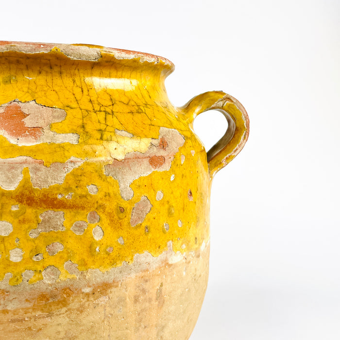 French country confit pot in terracotta, dating to the 19th century, with a generous rounded body and small side handles. The yellow ochre glaze shows heavy craquelure, chips, and glaze loss that reveal the warm clay underneath. This antique French jar is ideal for French country decor, farmhouse decor, and rustic kitchen styling where aged pottery adds depth and warmth.