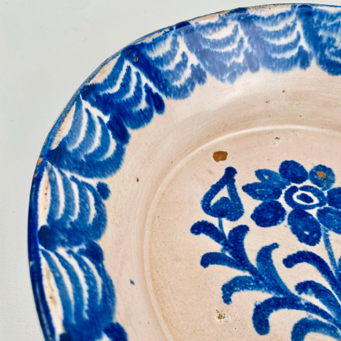 Close-up of the central floral bouquet motif on an antique Spanish lebrillo bowl, revealing layered cobalt brushstrokes, glaze pooling, and soft cobalt bleed into the tin glaze. This Granada pottery piece works as wall hanging ceramic decor or a serving bowl on open shelving, ideal for Wabi Sabi decor and Japandi interiors focused on authentic surface character.