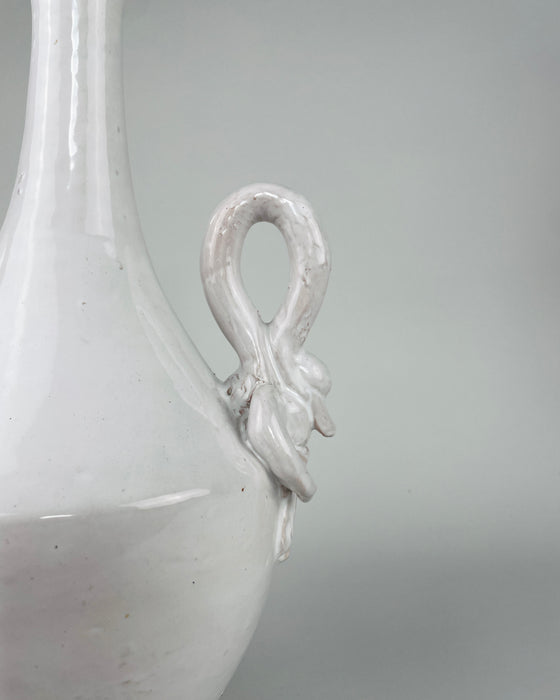 Applied ceramic swan ornament on the vintage Italian vase, showing the bird’s long neck, modeled head, layered wings and lower feather details beneath the glossy ivory white glaze. Small glaze losses, firing marks and darker clay traces remain visible around the relief, documenting the finished surface and age of the sculptural handle.