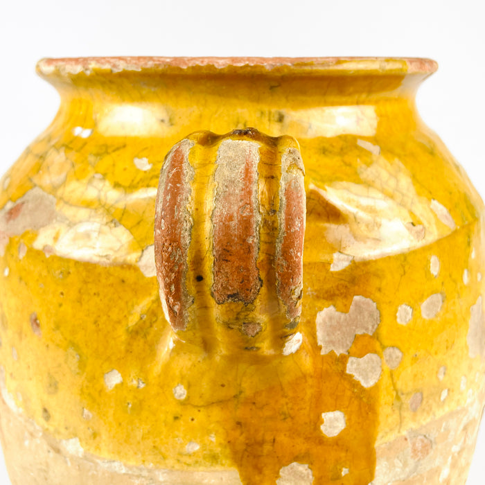 Antique French pottery confit pot with weathered yellow glaze, an earthenware jar from the French rural tradition of preserving food. The vessel features a rolled rim, twin loop handles, and a softly tapered base, with visible handmade variation and patina. Its timeworn finish gives it strong decorative value for Mediterranean decor, antique home decor, and rustic interiors.