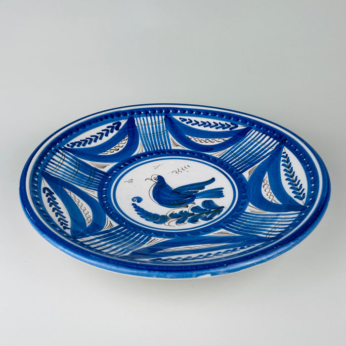 Large Spanish blue bird plate in hand painted Talavera faience, with a white tin glazed ground and a broad cobalt border arranged in alternating leaf shapes, gridded panels, dotted bands, and fine brown scrolls. The shallow charger form and graphic bird motif make this antique pottery a substantial piece of Spanish wall decor.