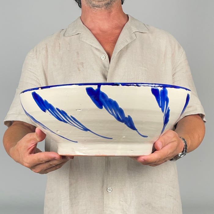 Spanish Fajalauza wall hanging bowl in glazed earthenware, decorated with a cobalt blue sunflower, curved stems, leaf forms, and concentric wavy lines across a white ground. The broad circular form and strongly painted rim make the bowl visually effective when mounted on a wall or placed as a centerpiece. It complements Mediterranean decor, farmhouse decor, and collected blue and white pottery.