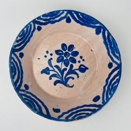 Ceramic plate with blue floral design on a white background. Antique style Granada Fajalauza lebrillo bowl, Spanish Andalusian pottery, featuring cobalt blue floral decoration and border brushwork over a pale tin-glazed surface. The back shows a hanging wire attached near the rim, supporting wall mounting. Condition includes glaze wear and terracotta exposure at the rim. Suitable for farmhouse decor and vintage kitchen display.