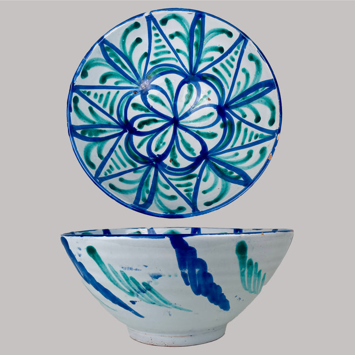 Vintage Fajalauza pottery bowl from Granada, Spain, a tin glazed terracotta lebrillo with opaque white glaze and hand-painted cobalt blue and copper green decoration. The interior shows a radial rosette with geometric vegetal panels, while rim wear and chips expose terracotta, suitable for Mediterranean decor serving and display.