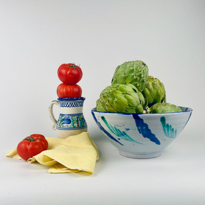 Decorative bowl with artichokes and tomatoes on a white background. Spanish Fajalauza decorative bowl associated with Granada pottery tradition, tin glazed terracotta painted in cobalt blue and copper green. The bowl works as functional tableware for tapas or bread and as wall hanging ceramic decor due to pierced holes near the rim area in wabi sabi, farmhouse Decor or japandi interiors. 