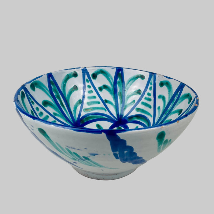 Vintage Fajalauza ceramic bowl from Granada, Spain, a tin glazed terracotta lebrillo with opaque white glaze and hand-painted cobalt blue and copper green decoration. The interior shows a radial rosette with geometric vegetal panels, while rim wear and chips expose terracotta, suitable for Mediterranean decor serving and display.