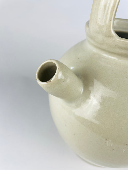 French terracotta water cruche with a narrow applied spout projecting from the upper shoulder between two handles. The cream glaze pools and changes tone around the handmade join, with an old hairline and small glaze losses visible at the attachment; this age detail is part of the antique vessel’s condition.